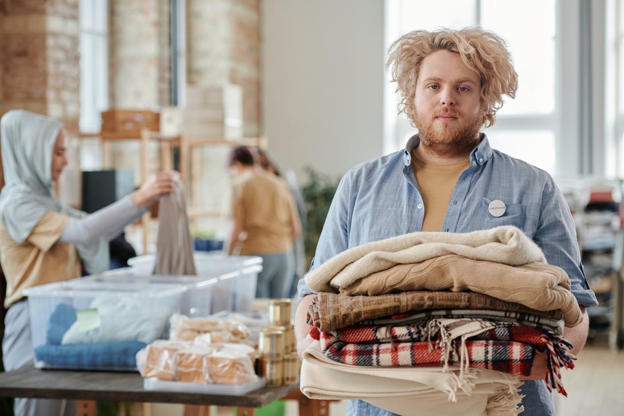 Mastering the First Impression: Your intriguing post title goes here A bearded man volunteers indoors, holding donated clothes for charity work amid a collaborative environment.